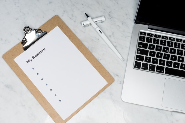 blank resume paper resting on a clipboard next to an open laptop